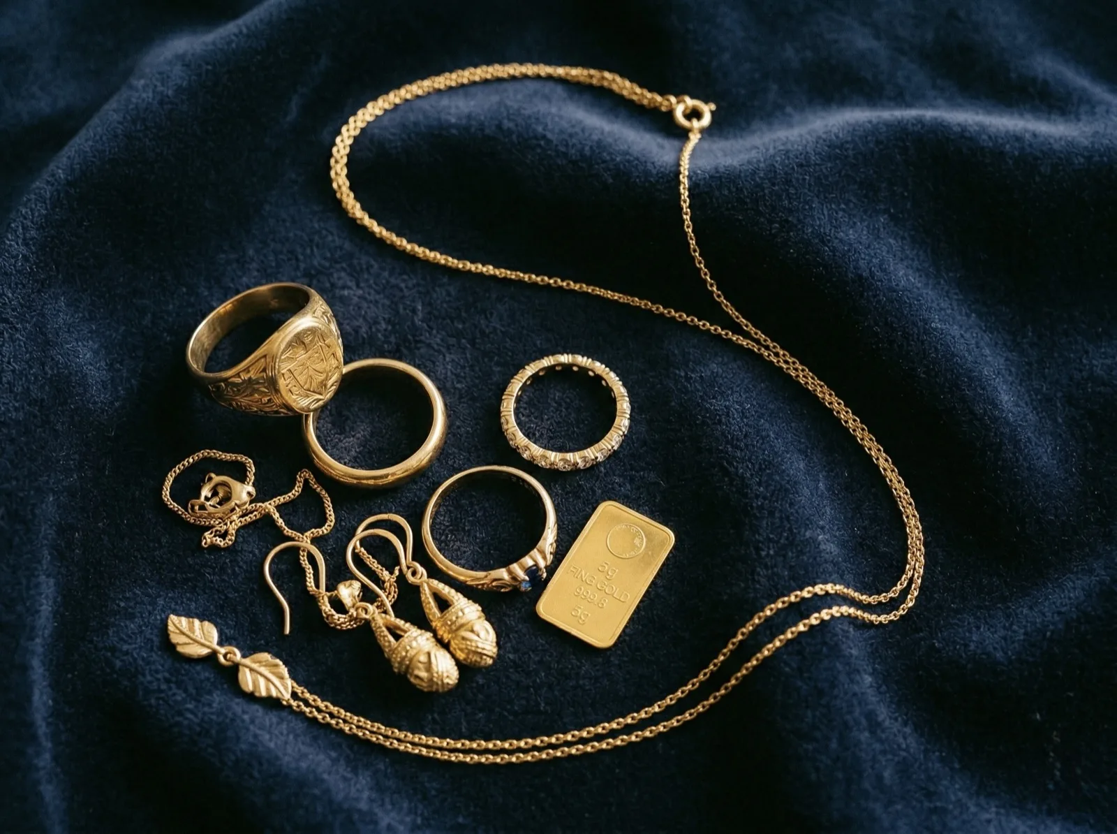 Gold rings, necklace, earrings and a gold bar arranged on dark velvet
